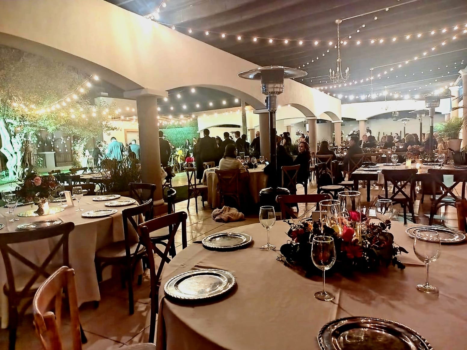 Cena en la terraza de arcos con series de luces y mesas redondas llenas